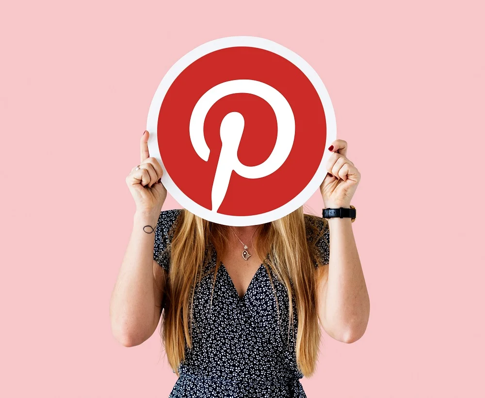 Woman holding Pinterest logo sign in front of face against a pink background